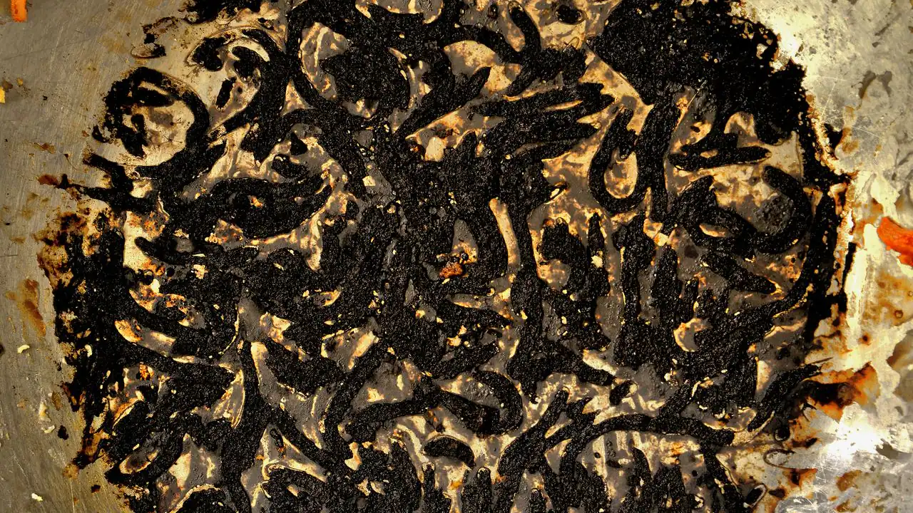 Burnt egg welded to a stainless steel pan on a stovetop — scorched protein is the hardest burnt smell to remove