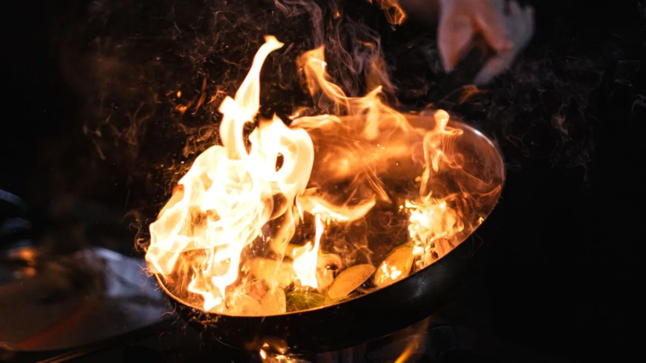 A pan of cooking oil engulfed in flames on a gas burner — the moment a grease fire starts and a metal lid becomes the fastest way to put it out