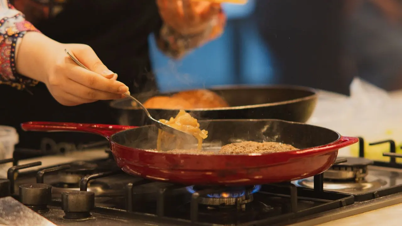 Meat cooking in a pan on a gas hob with smoke rising, the source of protein smoke residue in a kitchen